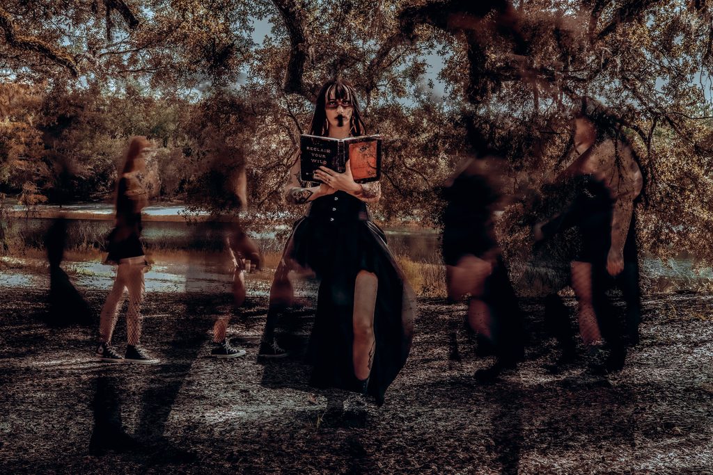 Dark fantasy model holding a book while ghostly shadow figures pass by in a cinematic witchy portrait in central florida.