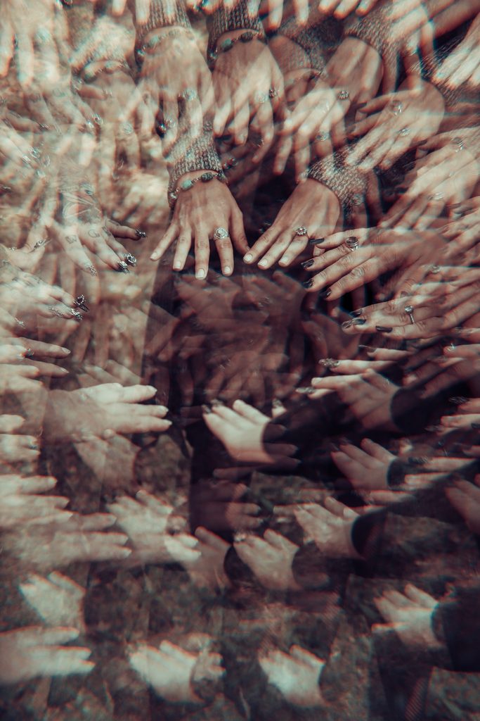 Prismatic lens distortion creating an atmospheric ring of overlapping hands and ethereal reflection in a dark fantasy portrait.