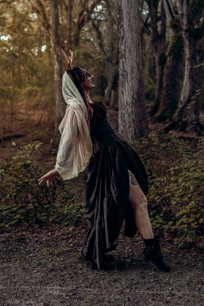 Ethereal dark fantasy model in flowing veil standing amongst woodland trees with atmospheric lighting